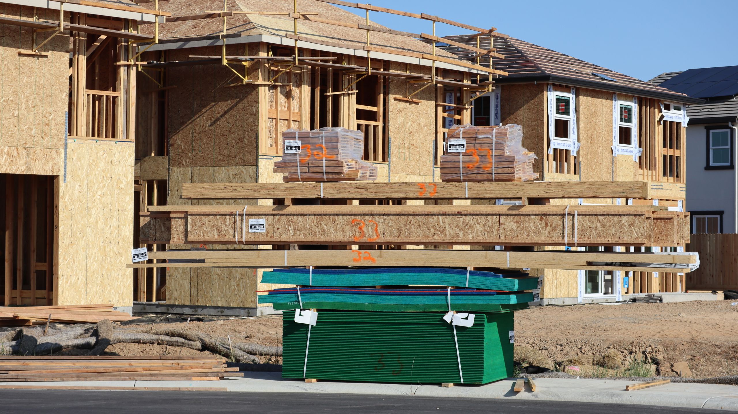 Stack of roofing materials including shingle bundles, underlayment rolls, and drip edge on a job site