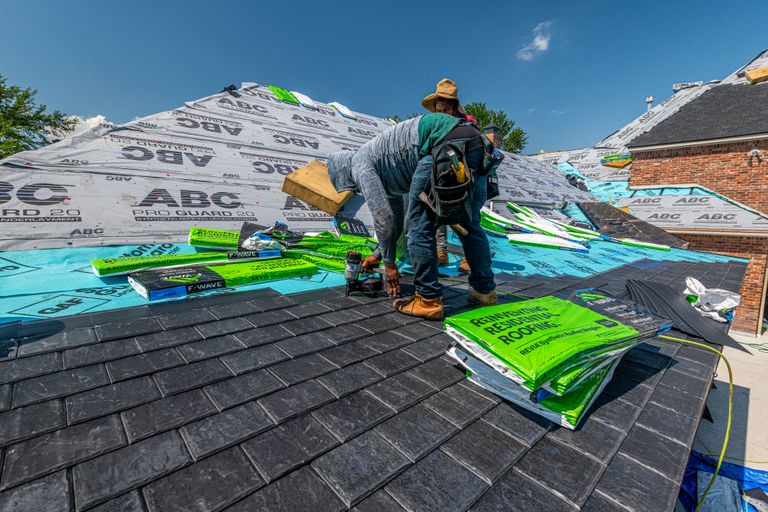 Roofer rolling out synthetic underlayment across a roof deck before shingle installation