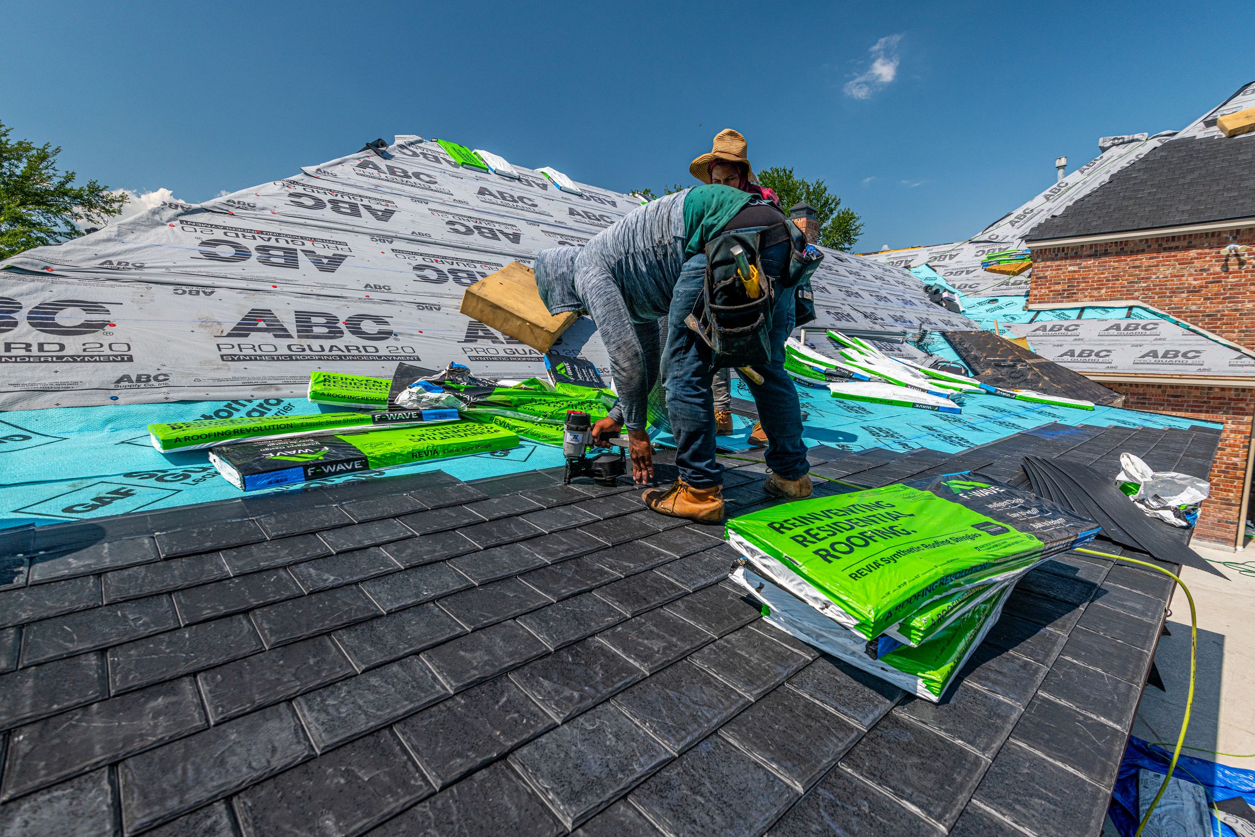 Roofer rolling out synthetic underlayment across a roof deck before shingle installation
